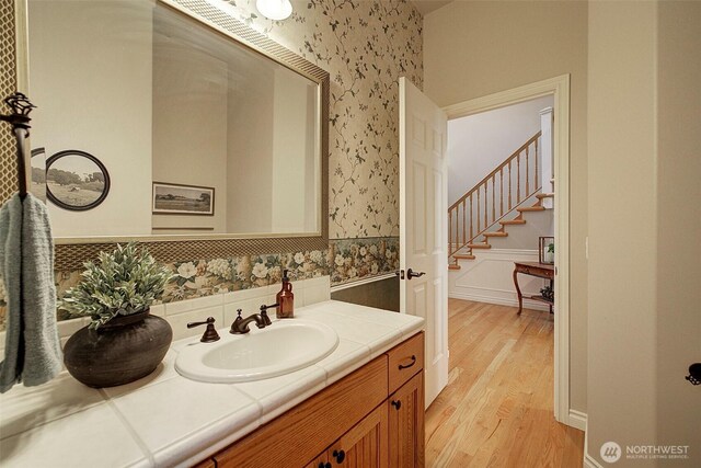 bathroom featuring wainscoting, wallpapered walls, vanity, and wood finished floors