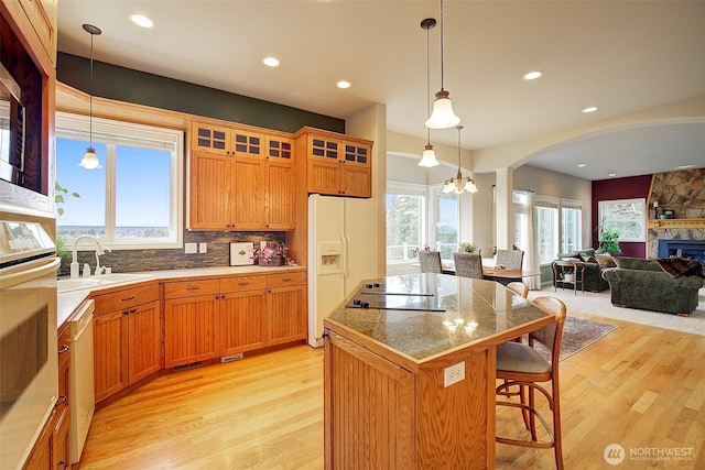 kitchen featuring a sink, a kitchen island, white appliances, a breakfast bar area, and glass insert cabinets