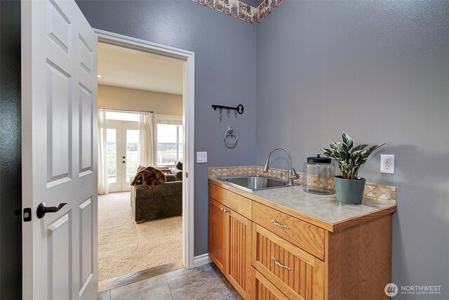 interior space with a sink, french doors, baseboards, and light colored carpet