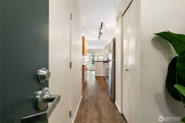 hall with dark wood-style floors, rail lighting, and baseboards