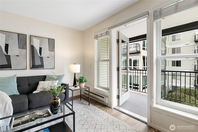 living area with a baseboard radiator, baseboards, a healthy amount of sunlight, and wood finished floors