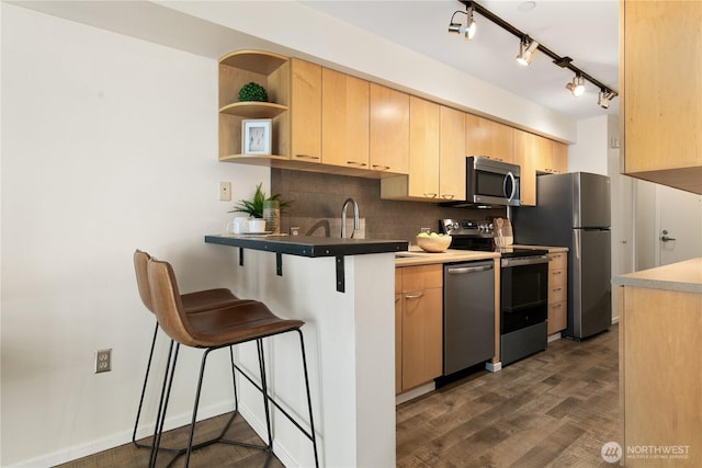 kitchen featuring tasteful backsplash, light brown cabinets, dark wood-type flooring, a breakfast bar area, and stainless steel appliances