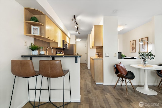 kitchen with dark wood-type flooring, stainless steel microwave, backsplash, a peninsula, and a breakfast bar area