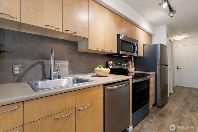 kitchen featuring light wood-type flooring, a sink, appliances with stainless steel finishes, light countertops, and decorative backsplash