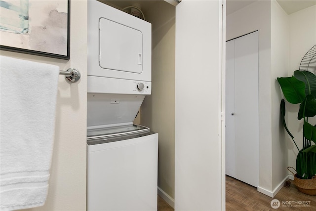 clothes washing area with laundry area, wood finished floors, stacked washer / drying machine, and baseboards