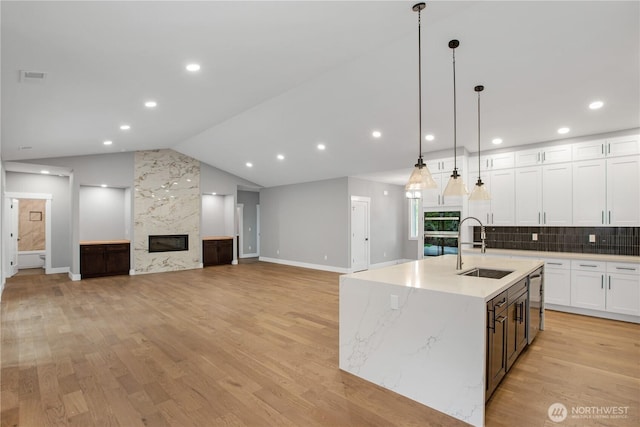 kitchen with a sink, light wood-style floors, white cabinets, a fireplace, and vaulted ceiling