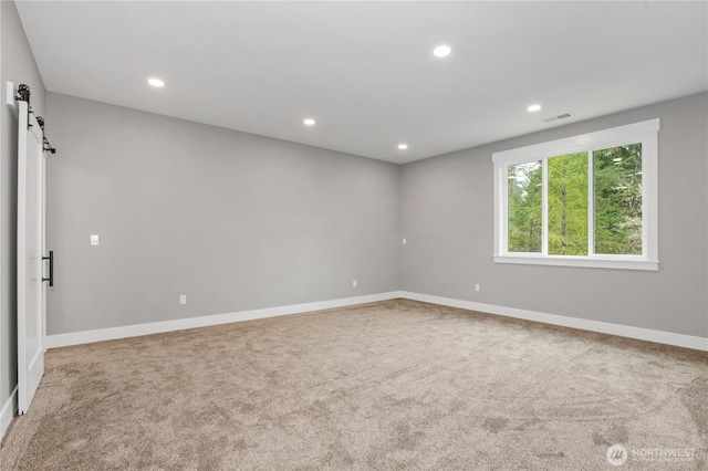 carpeted spare room with recessed lighting, a barn door, baseboards, and visible vents