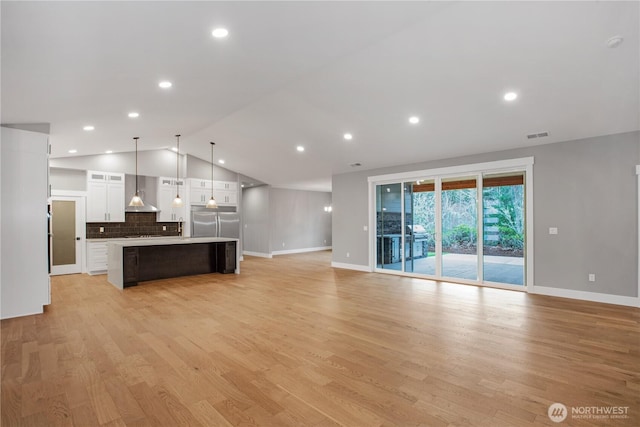 interior space with stainless steel refrigerator, open floor plan, white cabinetry, wall chimney range hood, and vaulted ceiling