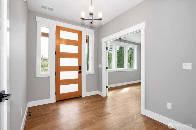 entryway featuring baseboards, wood finished floors, visible vents, and a chandelier