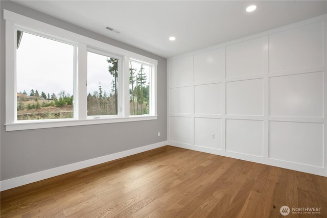 spare room with a decorative wall, visible vents, a wealth of natural light, and light wood-type flooring