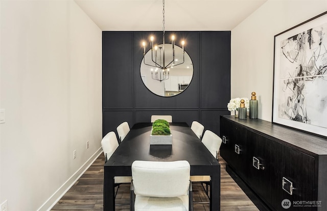 dining space with dark wood finished floors, a decorative wall, baseboards, and an inviting chandelier