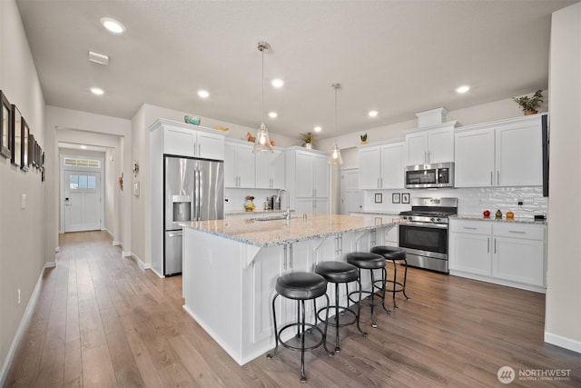 kitchen with a center island with sink, stainless steel appliances, decorative backsplash, white cabinetry, and light wood-type flooring