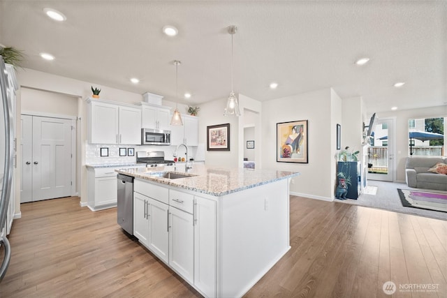 kitchen with open floor plan, appliances with stainless steel finishes, light wood-style floors, white cabinets, and a sink