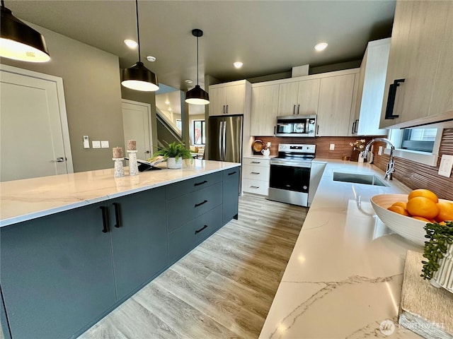 kitchen with light stone countertops, pendant lighting, appliances with stainless steel finishes, light wood-style floors, and a sink