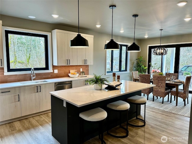 kitchen featuring a center island, light brown cabinetry, dishwasher, light wood-style floors, and a sink