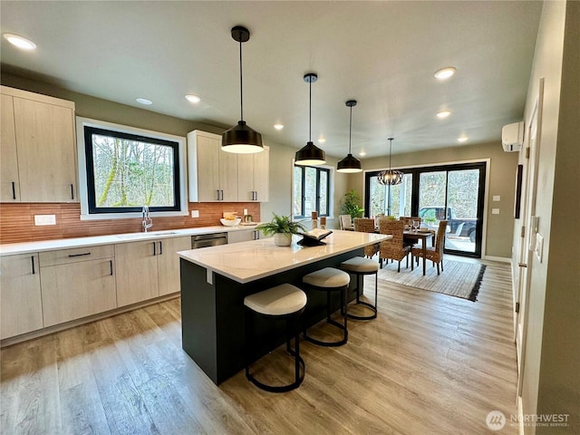 kitchen featuring a wall mounted AC, a kitchen island, a sink, light wood-style floors, and backsplash