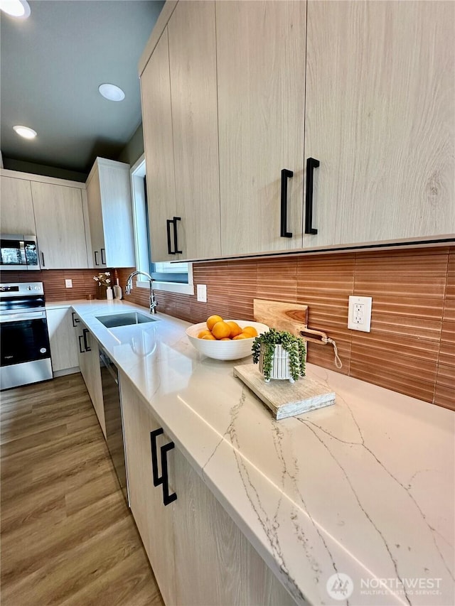 kitchen with a sink, light stone countertops, light wood-style floors, and stainless steel appliances