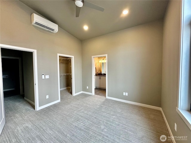 unfurnished bedroom with a wall mounted air conditioner, a walk in closet, lofted ceiling, carpet, and baseboards