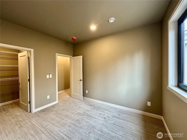 unfurnished bedroom featuring light carpet, multiple windows, a walk in closet, and baseboards