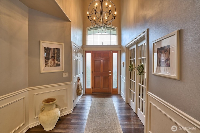 foyer with a decorative wall, a notable chandelier, dark wood-style floors, and wainscoting