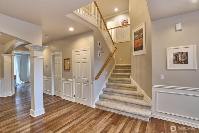 stairway with a wainscoted wall, arched walkways, wood finished floors, and ornate columns