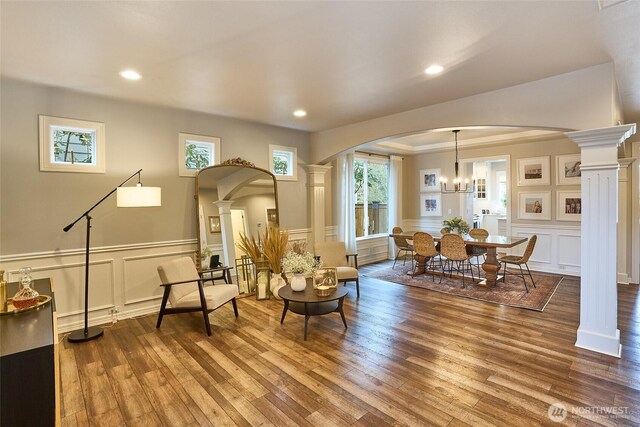 living area featuring decorative columns, arched walkways, wood finished floors, and a decorative wall