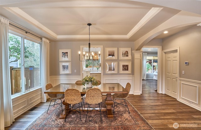 dining area featuring a tray ceiling, arched walkways, dark wood finished floors, and a decorative wall