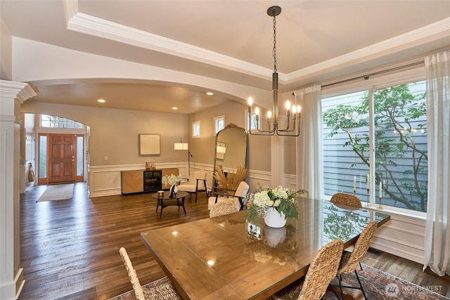 dining space with a wainscoted wall, arched walkways, ornamental molding, dark wood-type flooring, and a notable chandelier