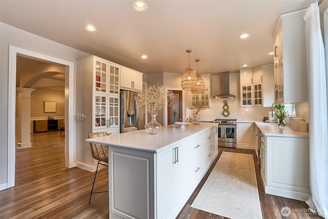 kitchen featuring wall chimney range hood, light countertops, arched walkways, stainless steel appliances, and a sink