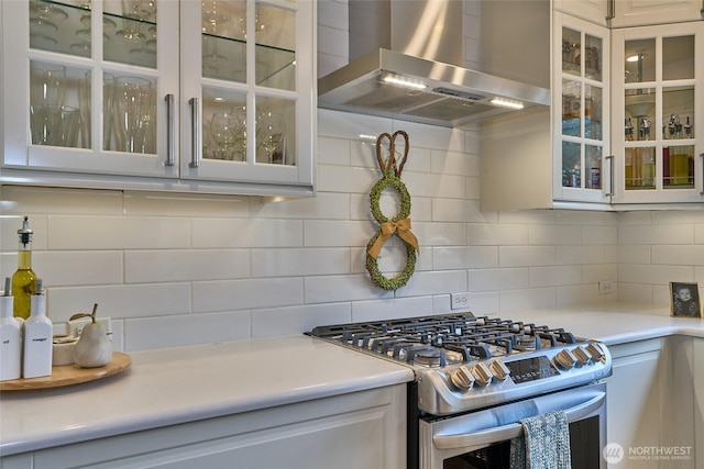 kitchen featuring gas stove, glass insert cabinets, tasteful backsplash, and wall chimney range hood