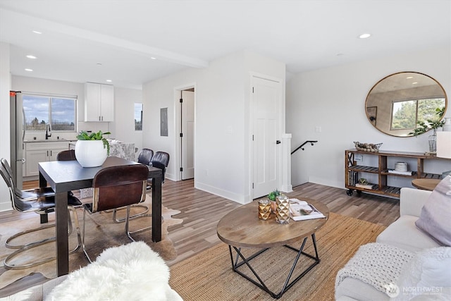 living area featuring beam ceiling, recessed lighting, baseboards, and light wood-style floors