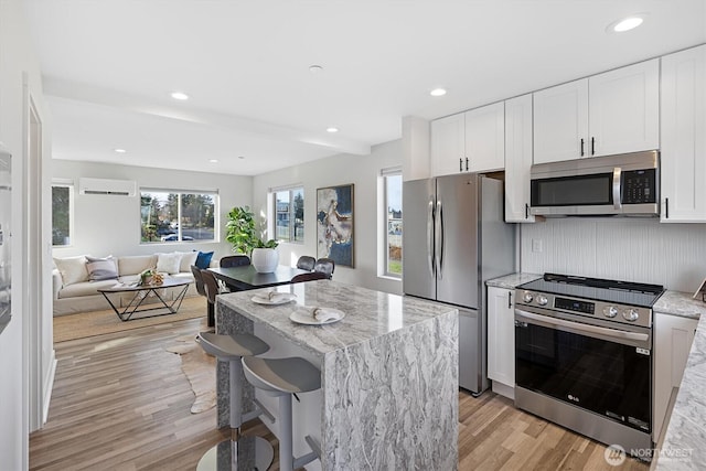 kitchen with light stone counters, appliances with stainless steel finishes, a kitchen island, and light wood-type flooring