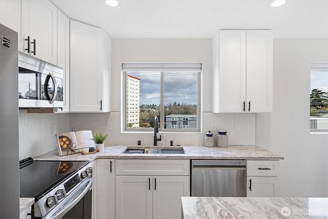 kitchen featuring a sink, light stone counters, appliances with stainless steel finishes, and white cabinets