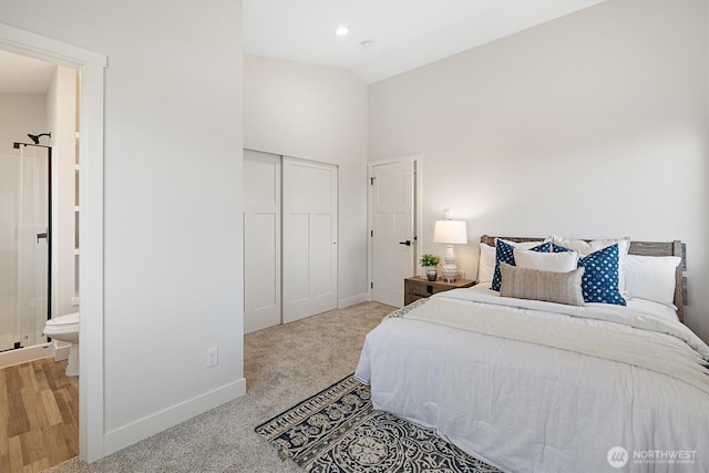 carpeted bedroom featuring a closet, ensuite bathroom, baseboards, and vaulted ceiling