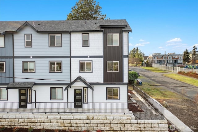 view of front of property with a residential view, a shingled roof, and fence