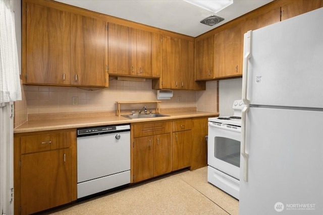 kitchen featuring a sink, white appliances, brown cabinets, and light countertops