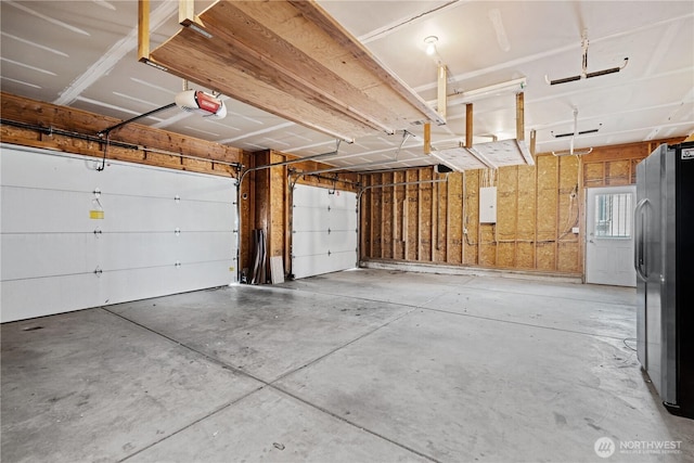 garage with electric panel, a garage door opener, and freestanding refrigerator