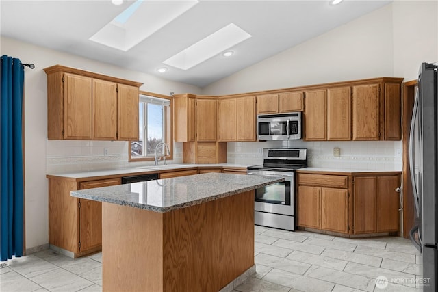 kitchen featuring a kitchen island, decorative backsplash, vaulted ceiling with skylight, stainless steel appliances, and a sink