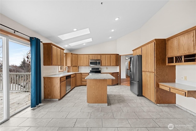 kitchen with a sink, a center island, stainless steel appliances, vaulted ceiling with skylight, and light countertops