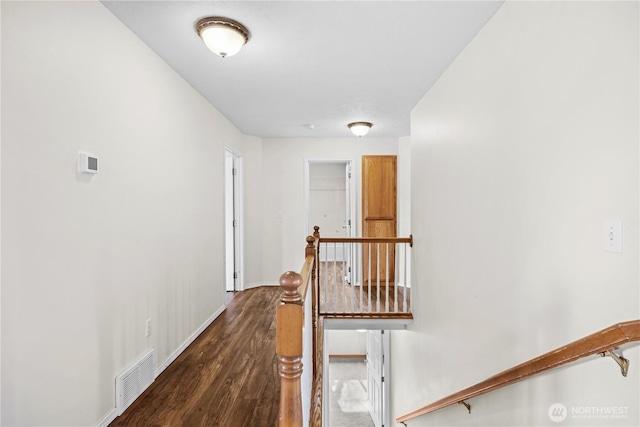 corridor featuring an upstairs landing, visible vents, baseboards, and wood finished floors