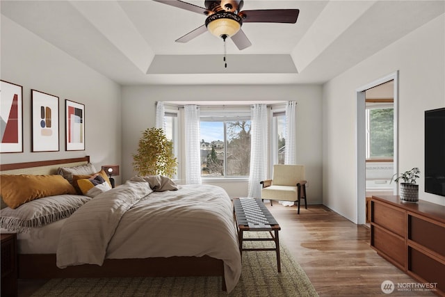 bedroom with a ceiling fan, light wood-type flooring, and a tray ceiling