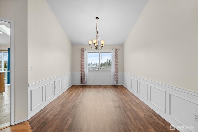 unfurnished dining area featuring vaulted ceiling, a notable chandelier, and wood finished floors