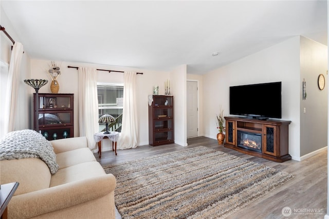 living room with a glass covered fireplace, lofted ceiling, baseboards, and wood finished floors