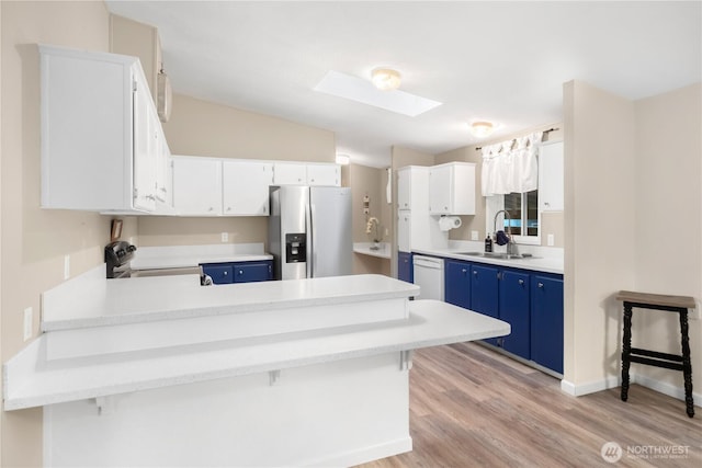 kitchen with a sink, blue cabinetry, white dishwasher, stainless steel fridge, and range