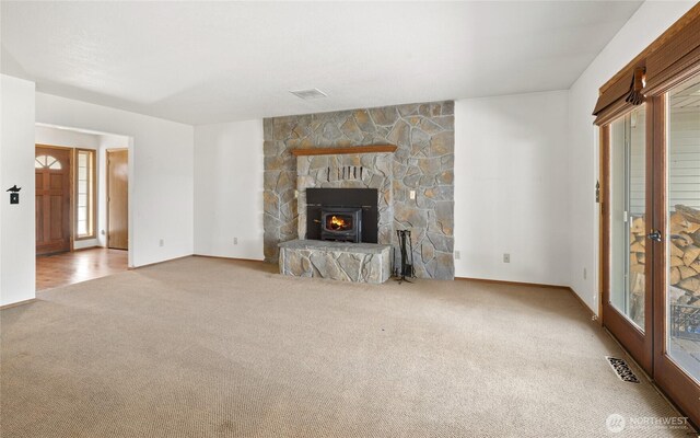 unfurnished living room with baseboards, visible vents, carpet floors, and a stone fireplace