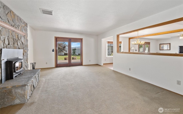 unfurnished living room with visible vents, a wood stove, a textured ceiling, carpet flooring, and a notable chandelier