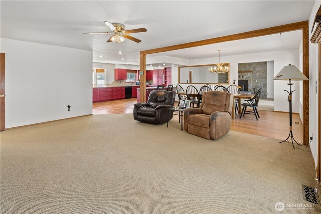 living area with visible vents, light carpet, a warm lit fireplace, and ceiling fan with notable chandelier