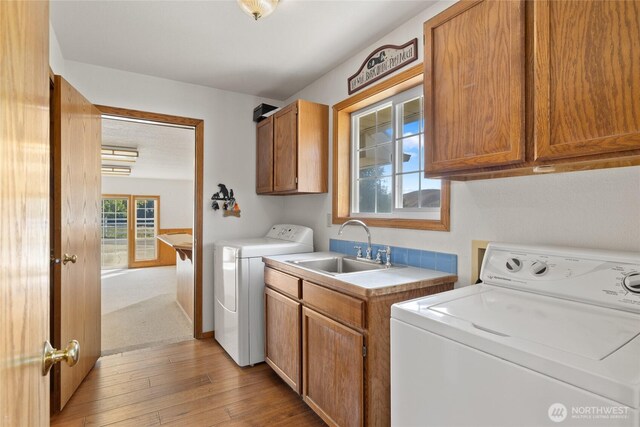 laundry area with washer and dryer, light wood-type flooring, cabinet space, and a sink