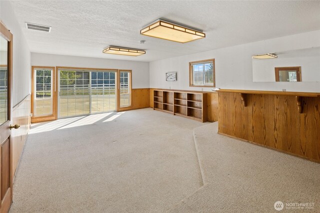 carpeted empty room with visible vents, a textured ceiling, wood walls, and wainscoting