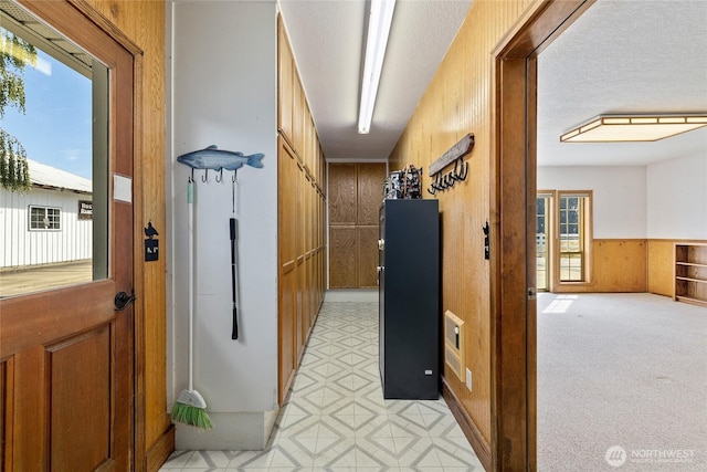 hall with a wainscoted wall, wood walls, a textured ceiling, and light floors